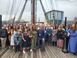 A happy group of people stand smiling aboard the deck of the RSS Discovery in Dundee